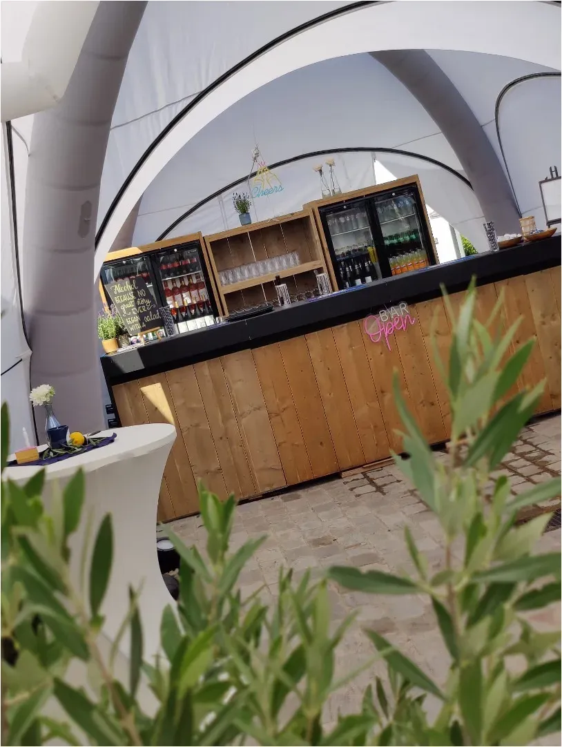 Een houten bar met koelkasten onder een pop-up tent van Soirée