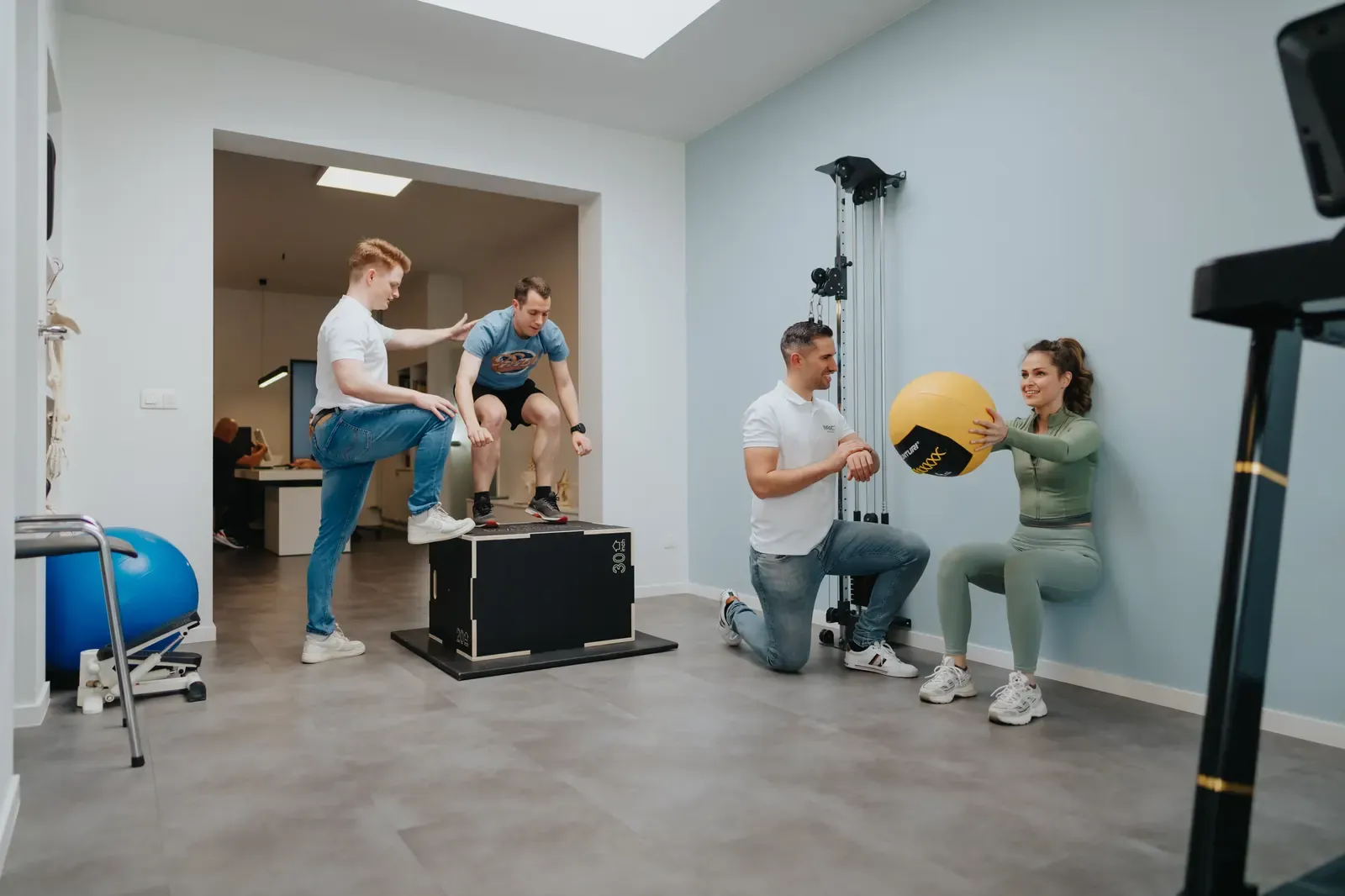 De oefenzaal van Impact Kinepraktijk, met een therapeut die een patiënte begeleidt bij een oefening met een medicijnbal