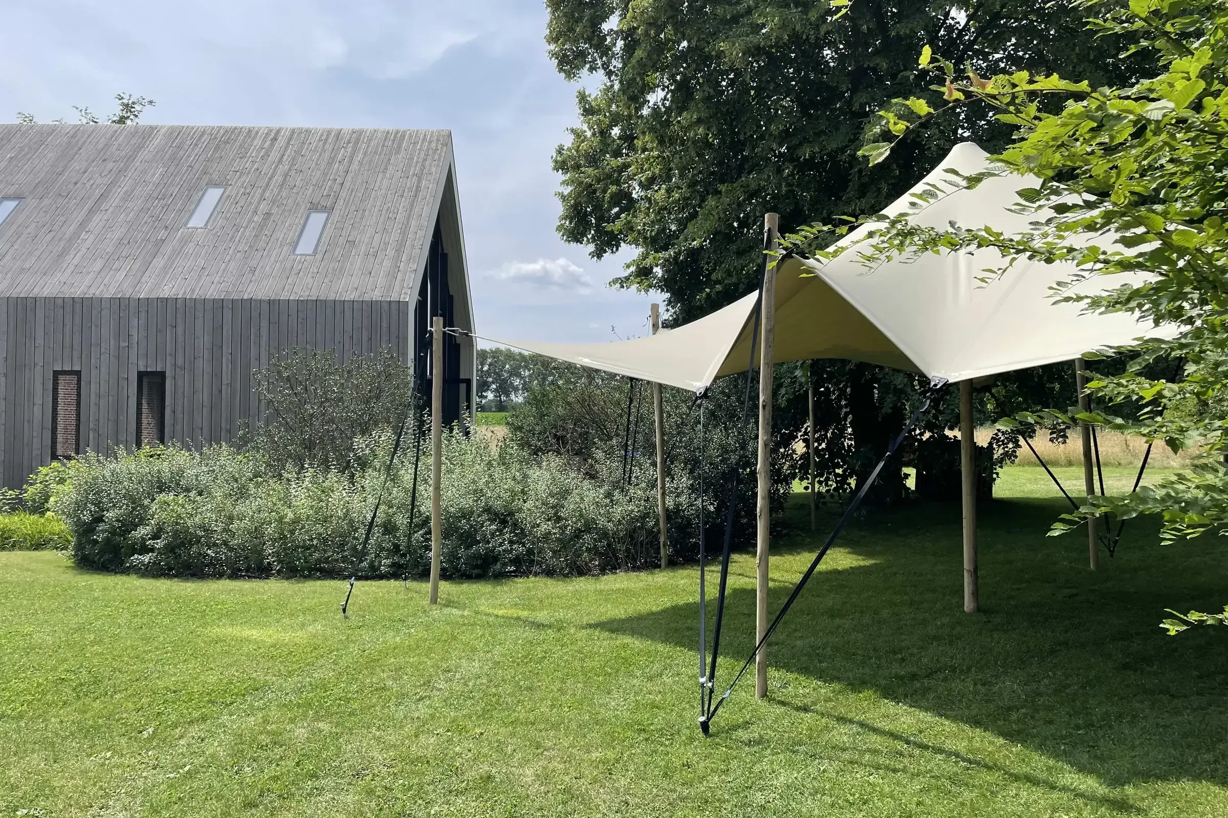 Een stretchtent van Soirée naast een moderne houten schuur, op een groen grasveld