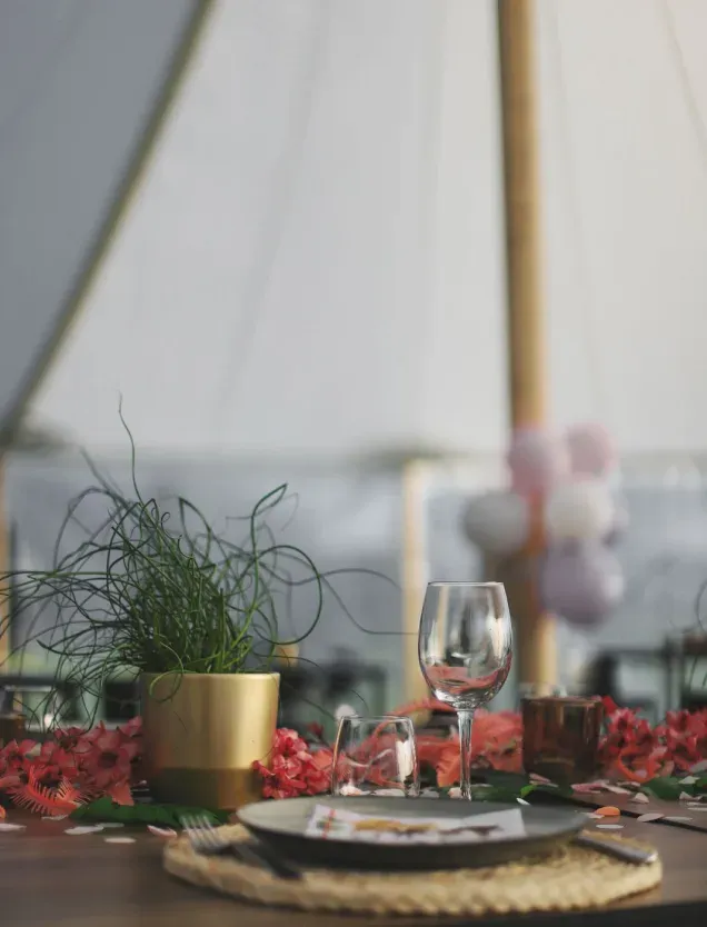 Een gedekte tafel met bloemen en een wijnglas onder een tent van Soirée